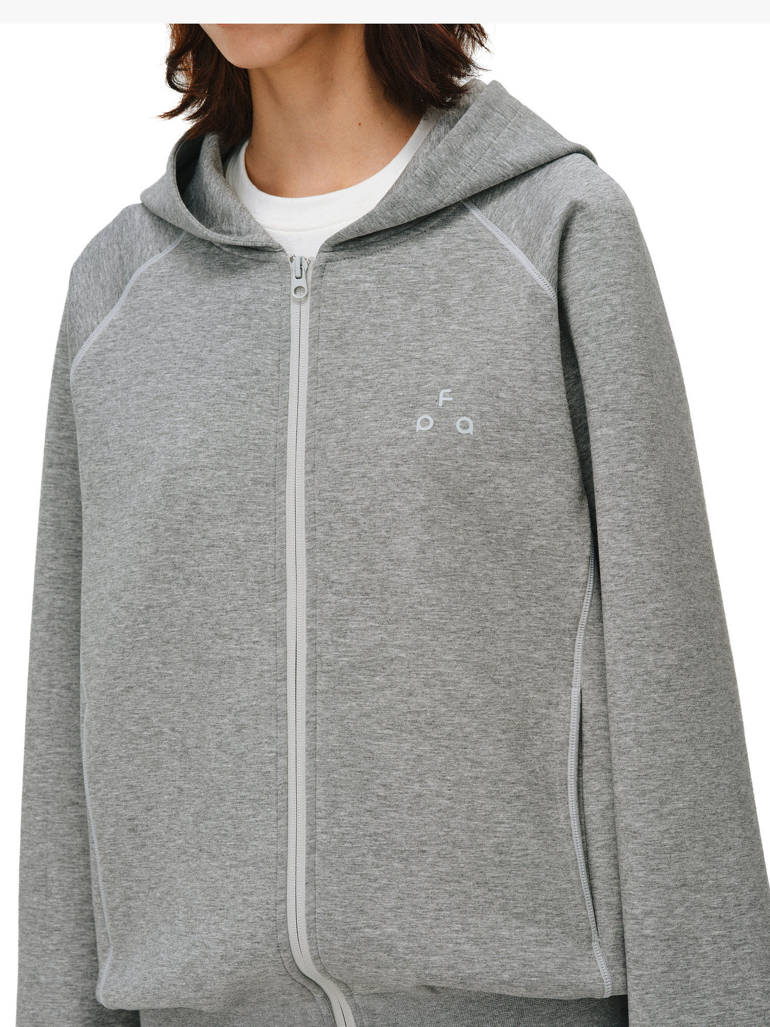 A person wears the EastLyst Constant Warmth Zip Hoodie in light gray, made from premium fabric with a hood and subtle white chest logo, layered over a white T-shirt. Their face is partially out of frame.