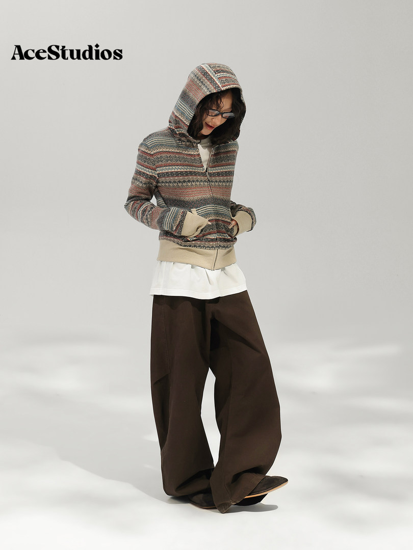 Model wearing a striped hooded knit sweater layered over a white top with wide-leg brown pants.