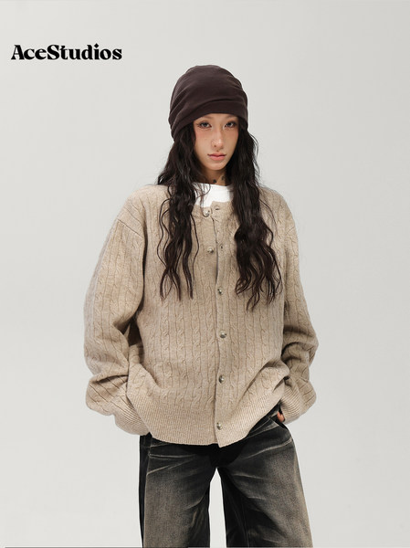 Model wearing a beige chunky knit cardigan with dark jeans and a brown knit hat.