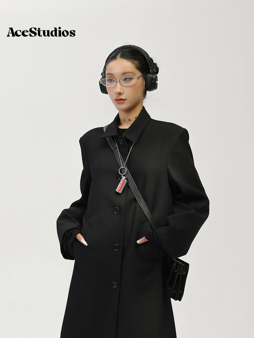 Model wearing a black tailored coat with headphones and a crossbody bag
