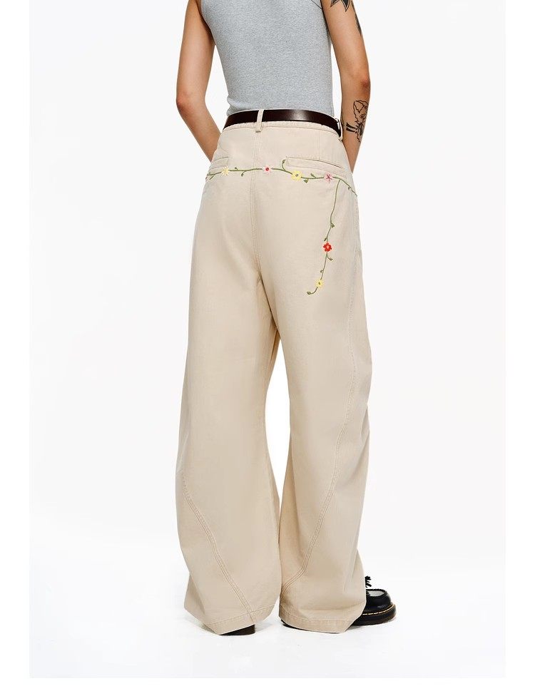 A person wears EastLyst Floral Embroidery Cargo Pants with floral embroidery on the back pocket, a black belt, gray sleeveless top, and black shoes, standing against a plain white background.