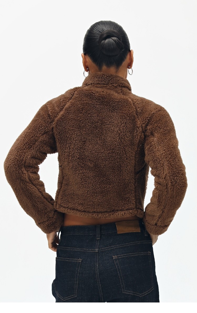 A person with dark hair in a bun, hoop earrings, and dark jeans is shown from the back wearing the EastLyst Pink Short Faux Shearling Jacket against a plain white background.