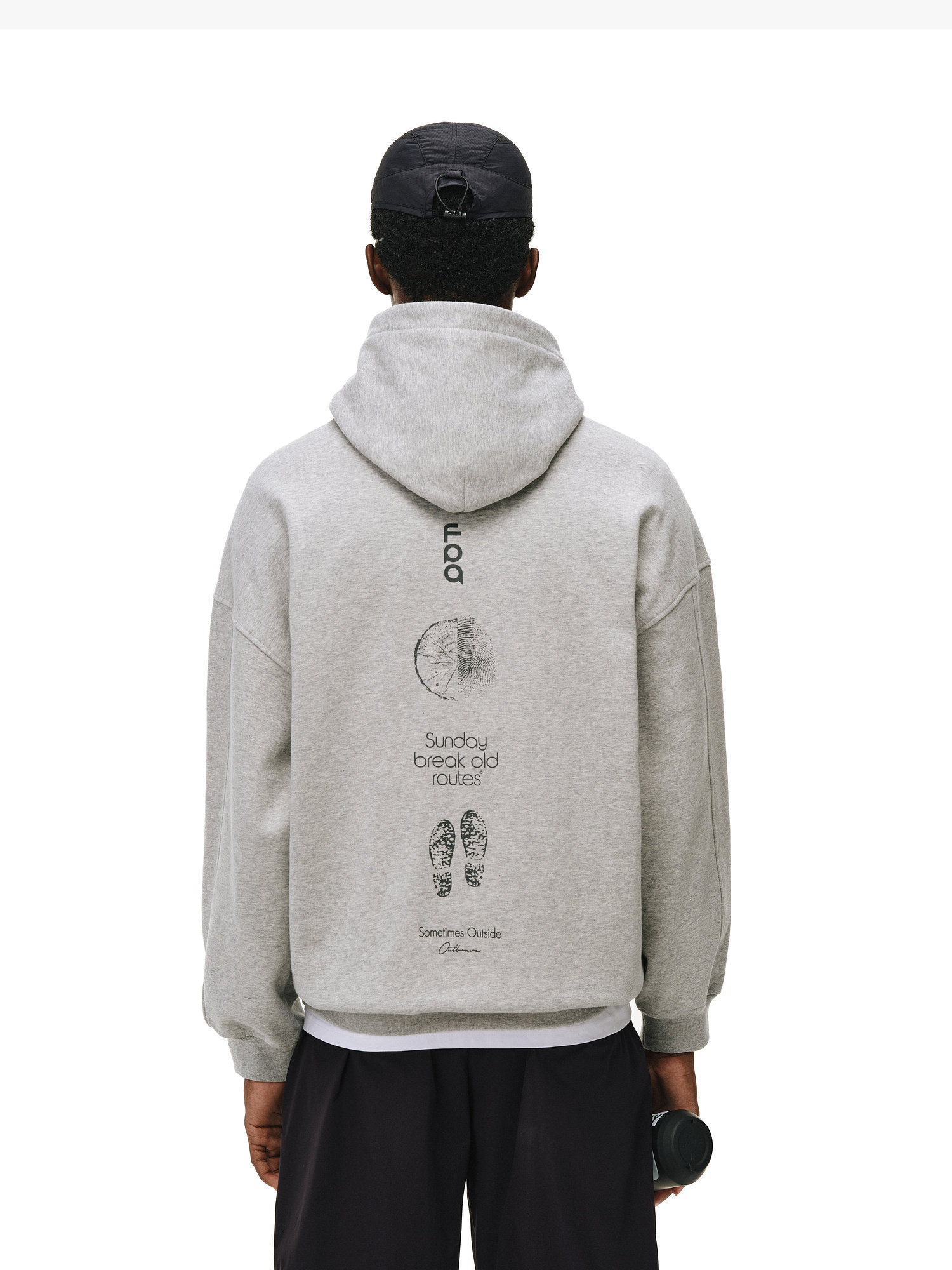 A person wears the EastLyst Outdoor Print Hoodie, a gray thermoregulating top with black graphics—featuring a clock, shoe prints, and "Sunday break old routes" text on the back—paired with a black cap and holding a water bottle.