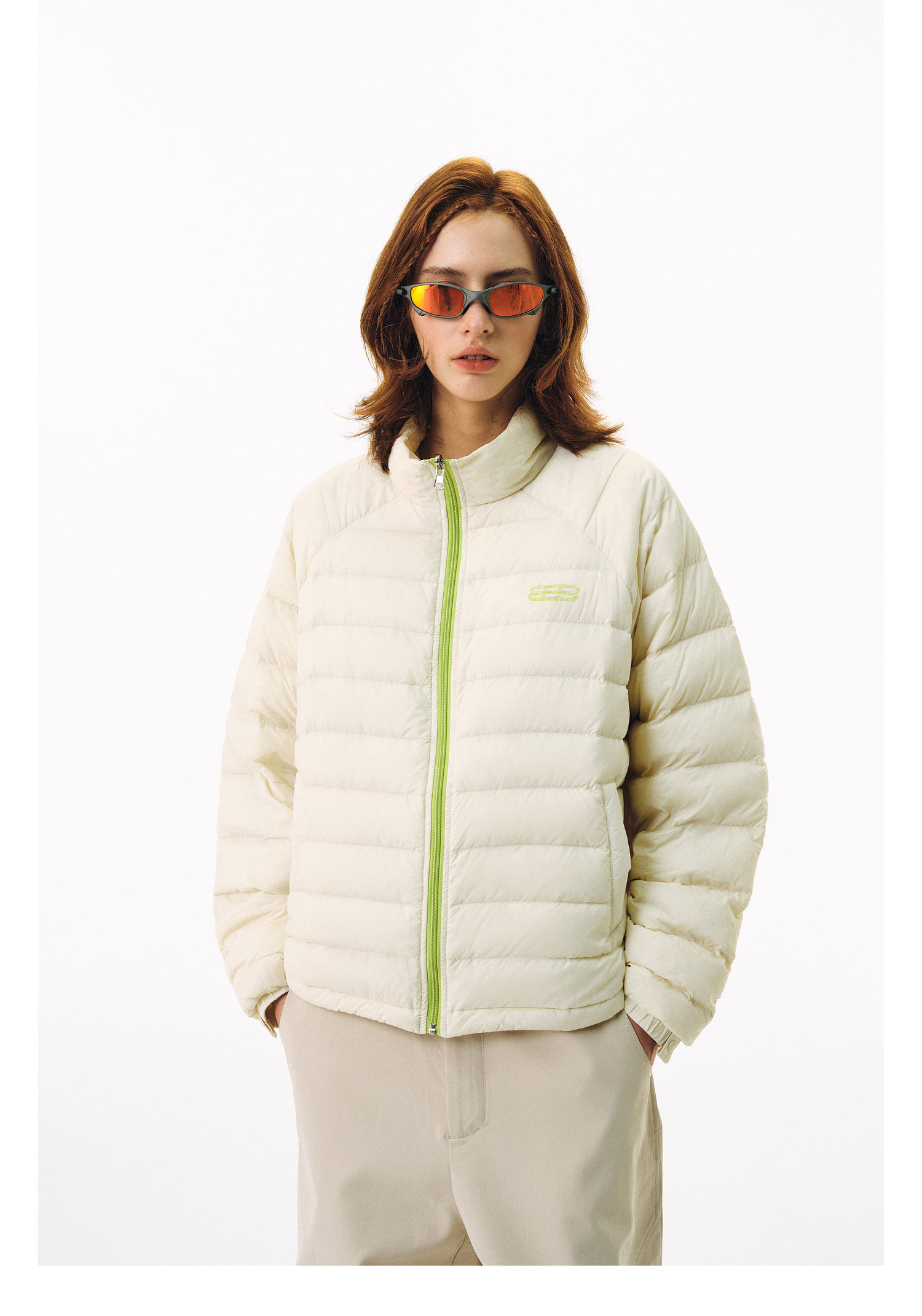 A person wears the EastLyst Versatile Explorer 3-in-1 Jacket in light beige with neon green accents, paired with reflective sunglasses and beige pants. The jacket’s waterproof shell stands out against a plain white background.