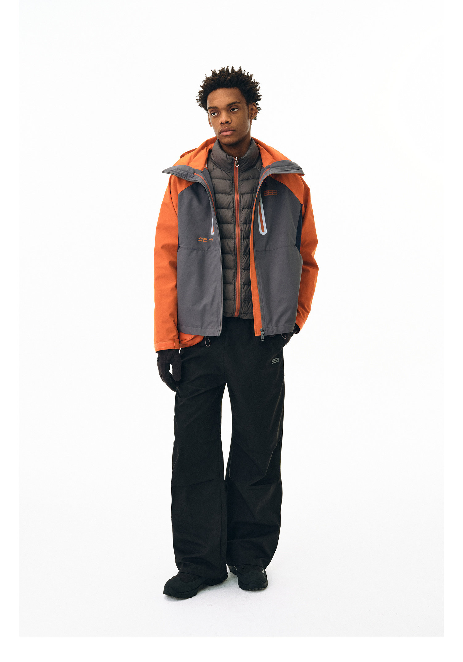 A person stands against a white background wearing the EastLyst Versatile Explorer 3-in-1 Jacket over black wide-leg pants, black gloves, and black shoes.