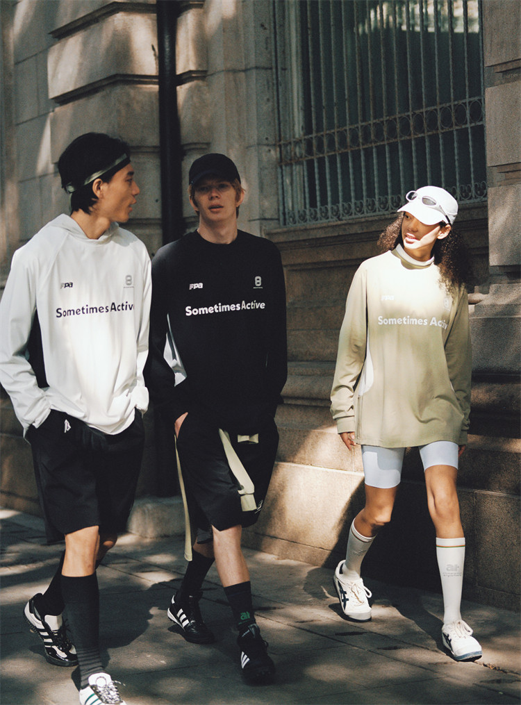 Three people stroll outside on a sunny day, wearing EastLyst Quick-Dry Color Block Long Sleeve Tees. Chatting as they walk by a stone building, they enjoy the comfort and style of their sporty shirts.