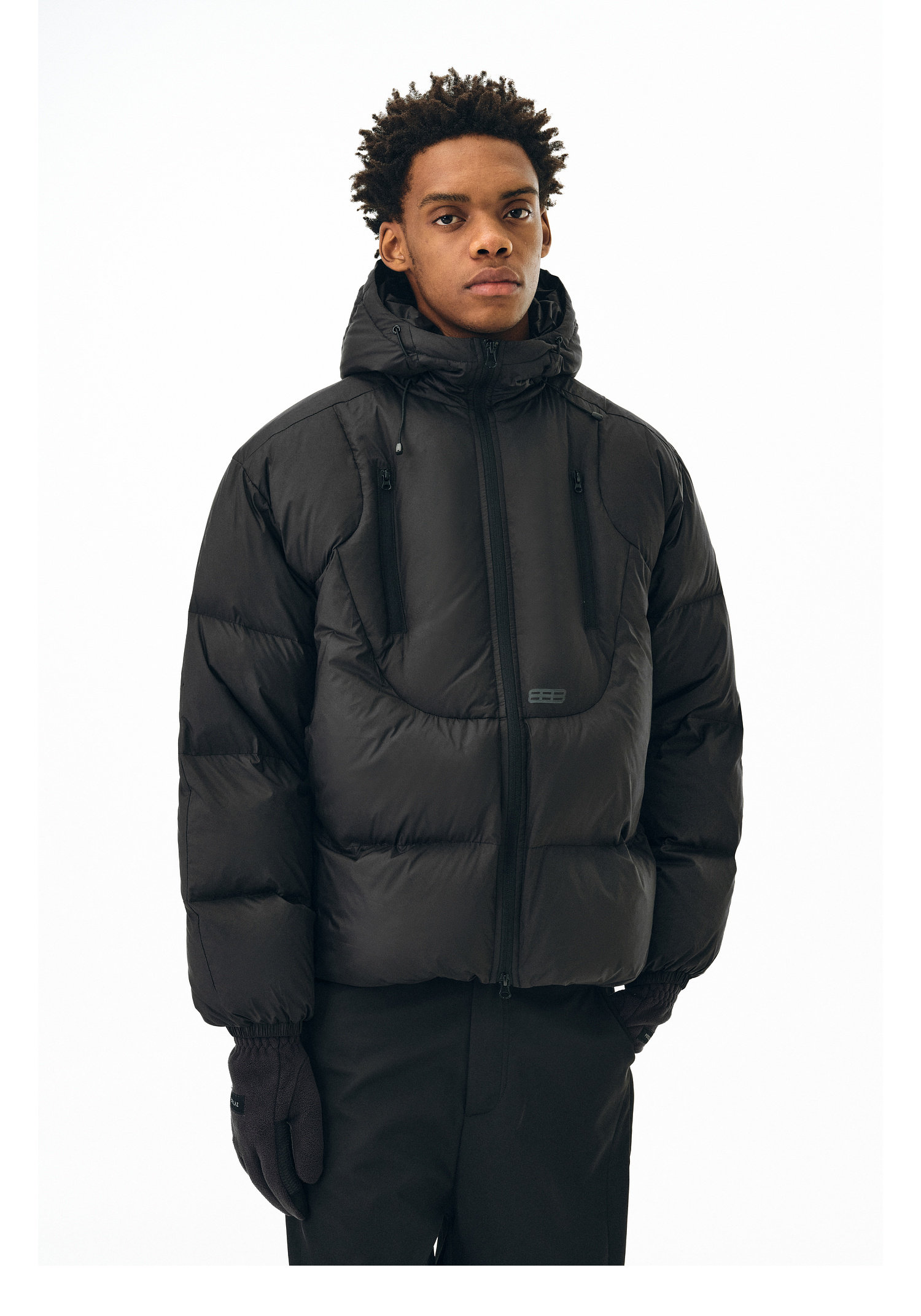 A person wears the EastLyst Fashionable 3D short down jacket in black, featuring a hood, standing facing forward against a plain white background. The winter jacket is zipped up, and the person displays a neutral expression.