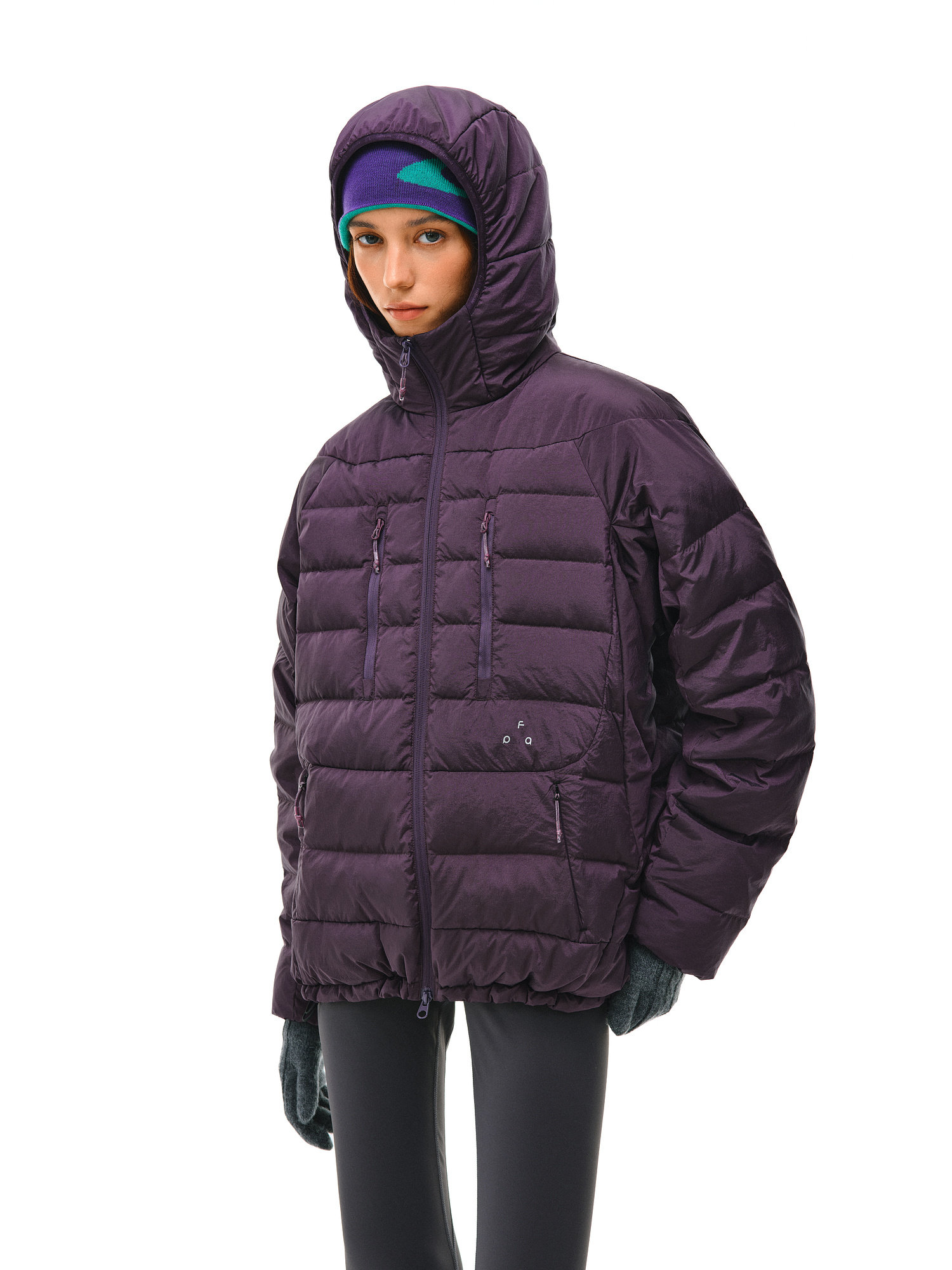 A person wears the EastLyst Dual-Zip Quilted Puffer Jacket in dark purple with a hood, paired with teal gloves and a blue headband, standing against a white background.
