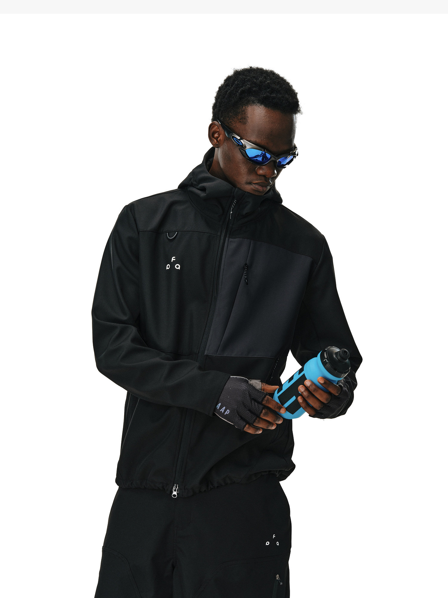 Wearing the EastLyst Color-Block Water-Resistant Softshell Jacket, black gloves, and sunglasses, a person holds a blue water bottle and looks down at it against a plain white background.