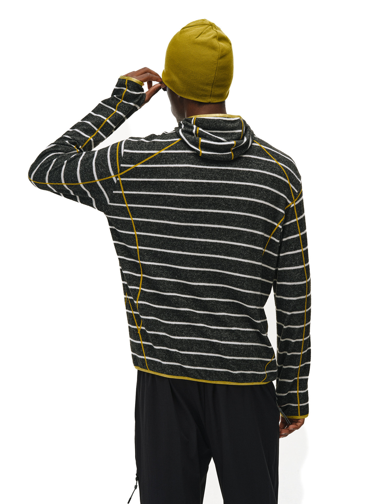 A person is seen from the back in an EastLyst Textured Stripe Knit Hoodie with black and white stripes and yellow seams, paired with a yellow beanie, against a plain white background for an effortlessly casual look.