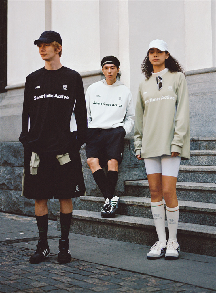 Three young adults wear EastLyst Quick-Dry Color Block Long Sleeve Tees, shorts, and sneakers as they stand and sit on stone steps outside, each sporting a cap and long socks in neutral tones.