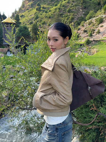 Woman modeling a beige jacket and dark shoulder bag outdoors