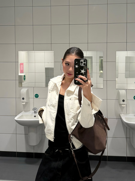 Woman wearing a white jacket and carrying a large brown shoulder bag in a restroom mirror selfie