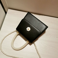 Стиль черной камелии дополнен длинной жемчужной цепочкой.