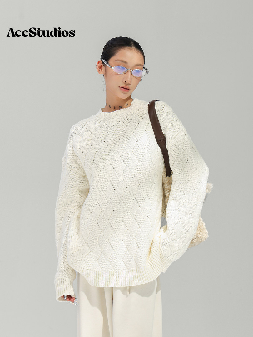 Model wearing a cream textured knit sweater with light trousers and a shoulder bag