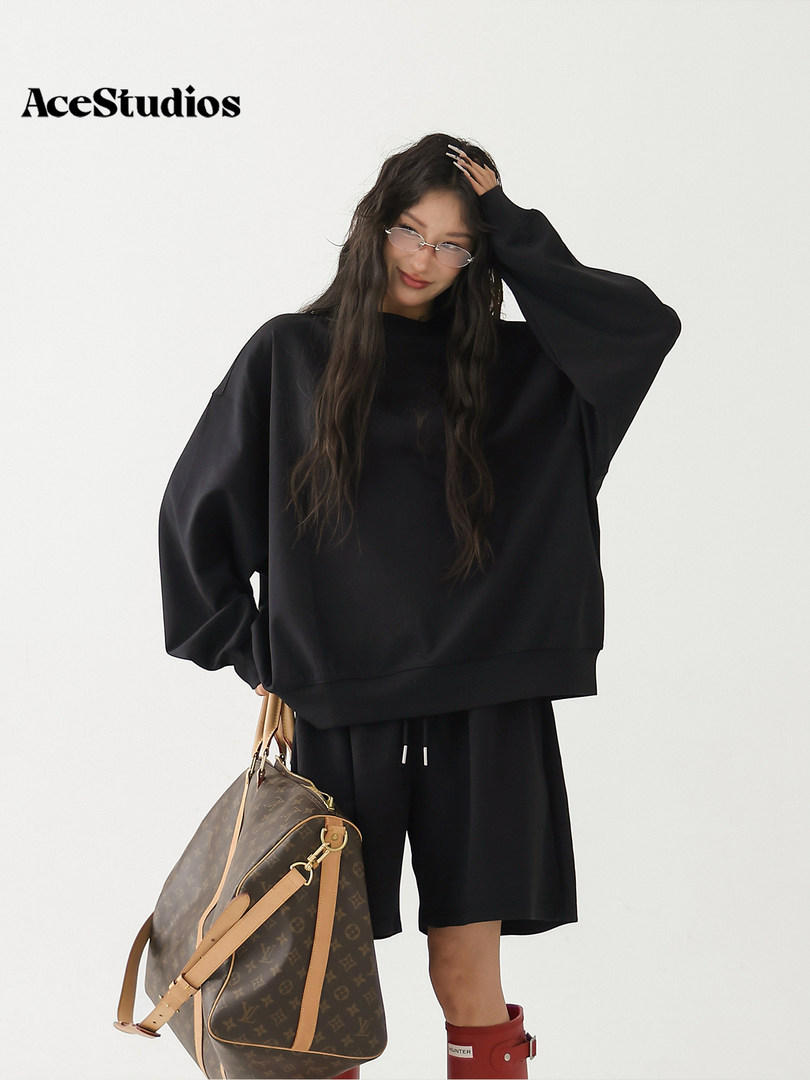 Model wearing an oversized black sweatshirt and shorts with a brown designer handbag.