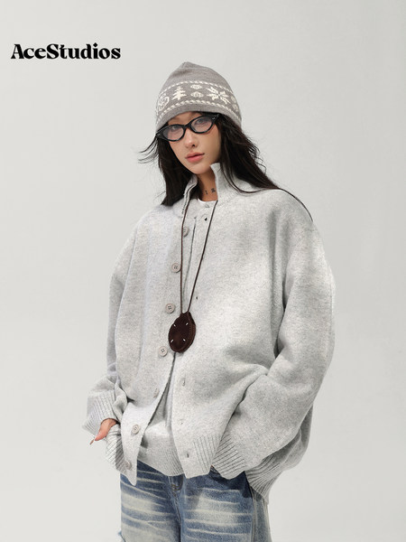 Model wearing a gray knit cardigan, patterned beanie, glasses, and jeans.
