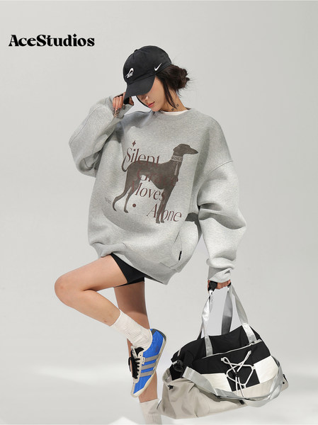Model wearing an oversized gray graphic sweatshirt with a black cap, sneakers, and carrying a large black-and-white tote bag.
