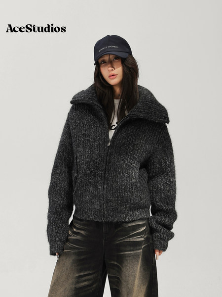 Model wearing a dark textured zip-up jacket with black pants and a cap