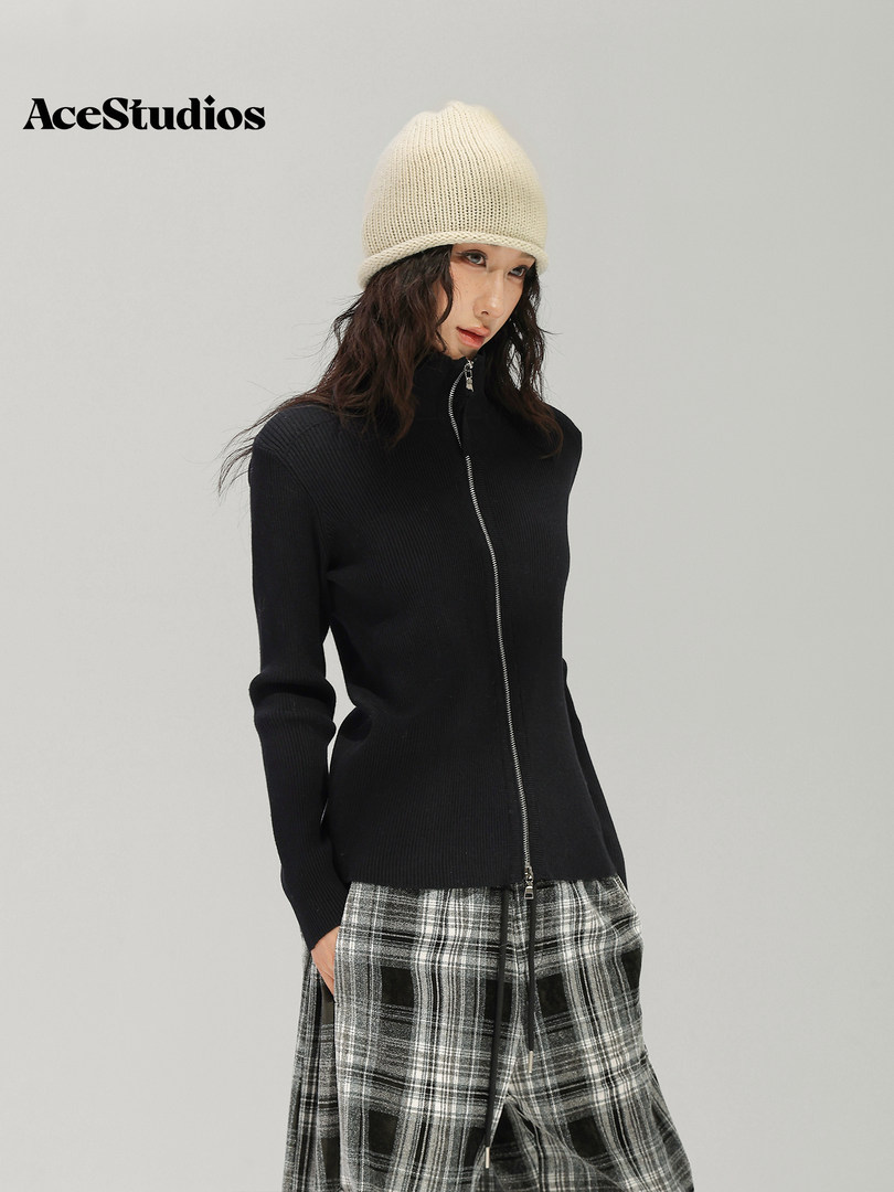 Model wearing a black zip-up knit top, plaid trousers, and a cream knit beanie.