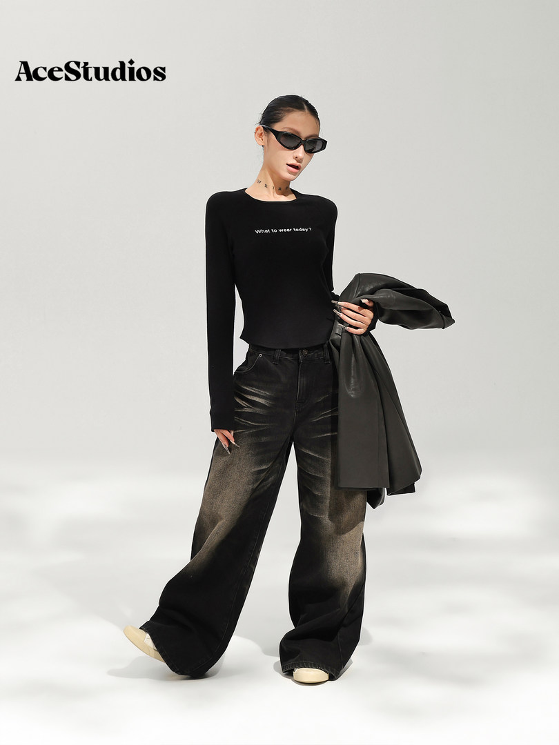 Model wearing a black fitted long-sleeve top and wide-leg pants with a draped coat.