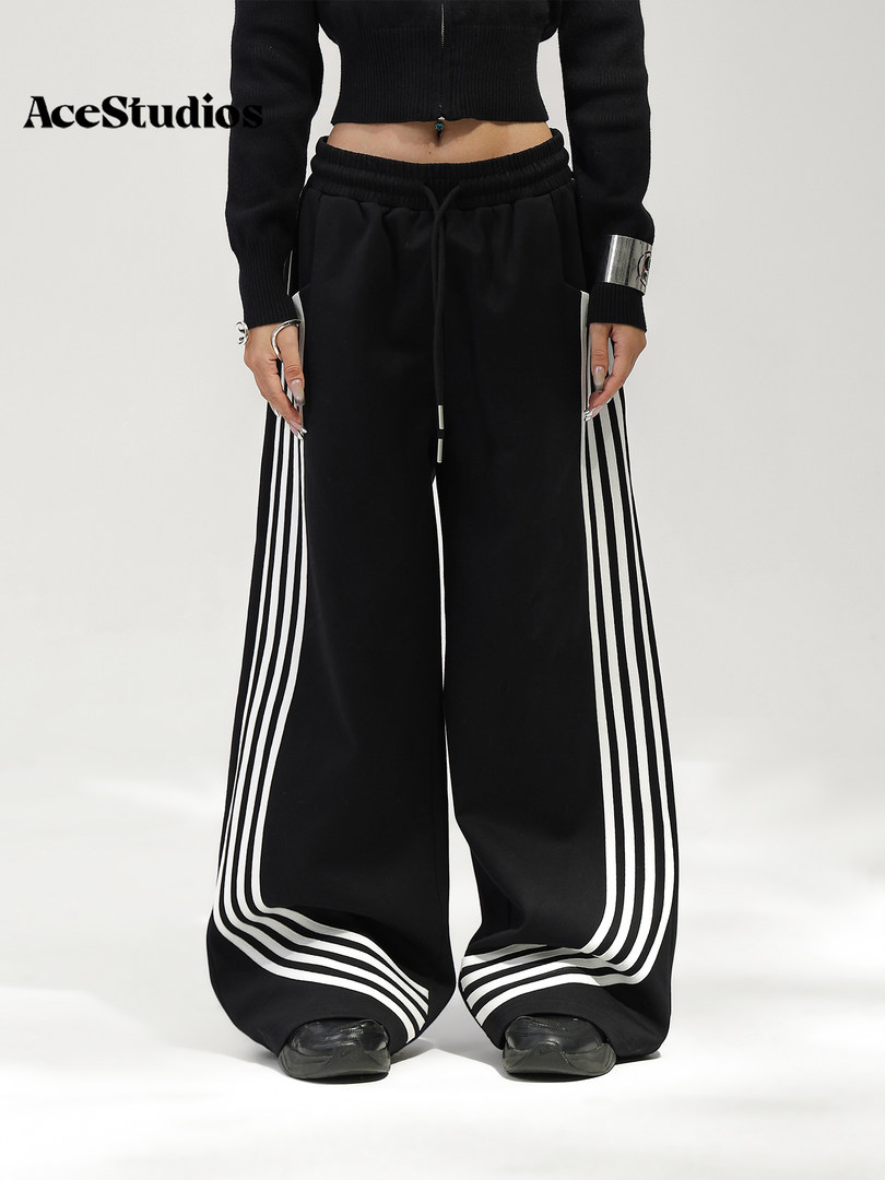 Black wide-leg track pants with white side stripes worn by a model.