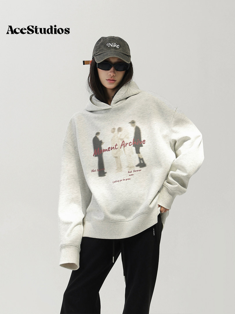 Model wearing an oversized light gray graphic hoodie with black pants and cap