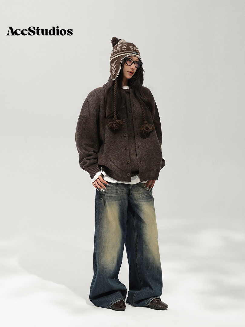 Model wearing a chunky brown knit sweater, patterned winter hat, and wide-leg distressed jeans.