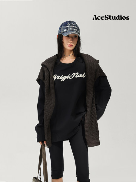 Model wearing a black layered streetwear outfit with cap and shoulder bag