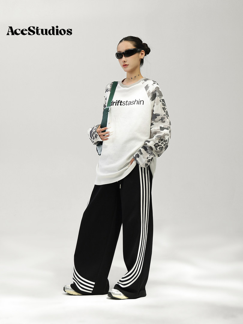 Model wearing a black-and-white streetwear outfit with a patterned long-sleeve top and wide-leg track pants.