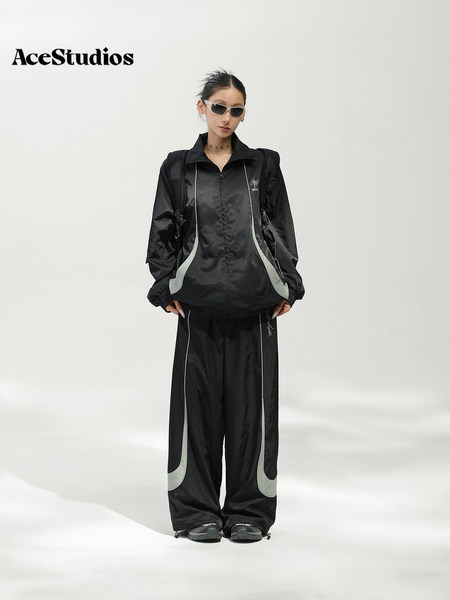 Model wearing a black sporty jacket and wide-leg pants set with reflective accents.