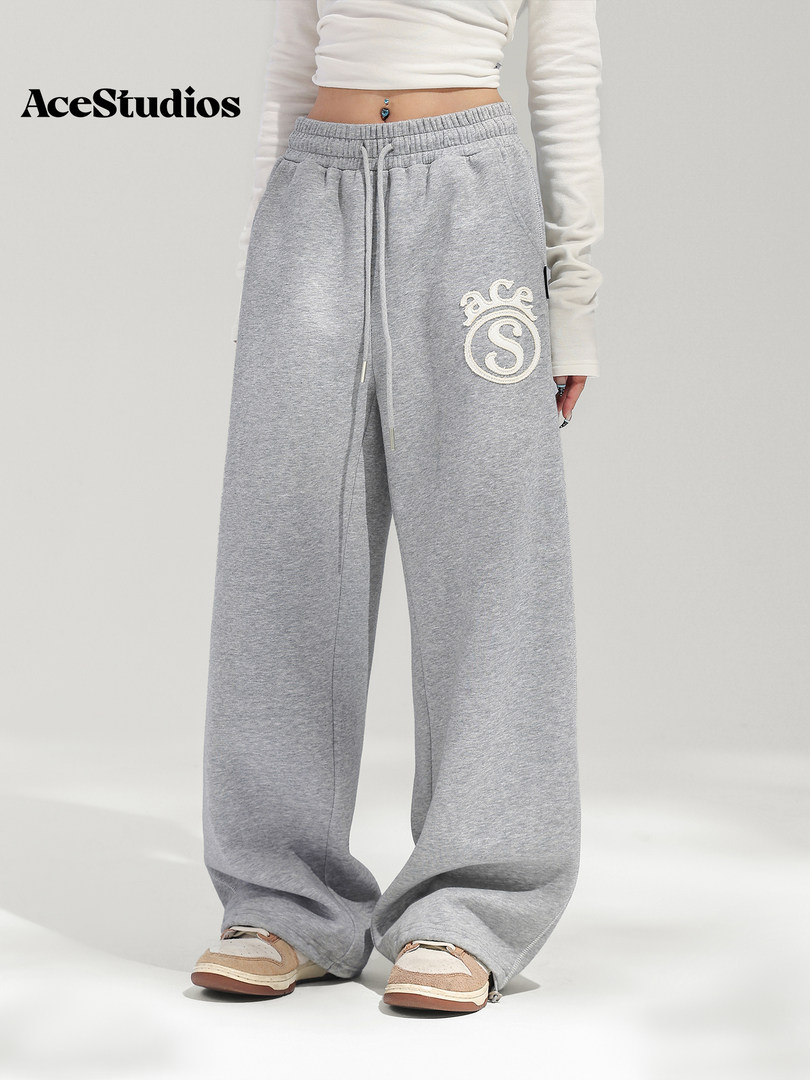 Model wearing loose gray fleece sweatpants with a white embroidered logo.