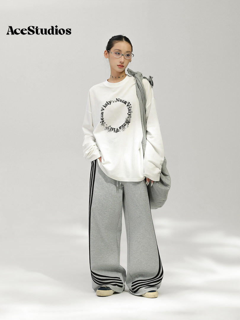Model wearing a white graphic sweatshirt with wide gray pants and sneakers.