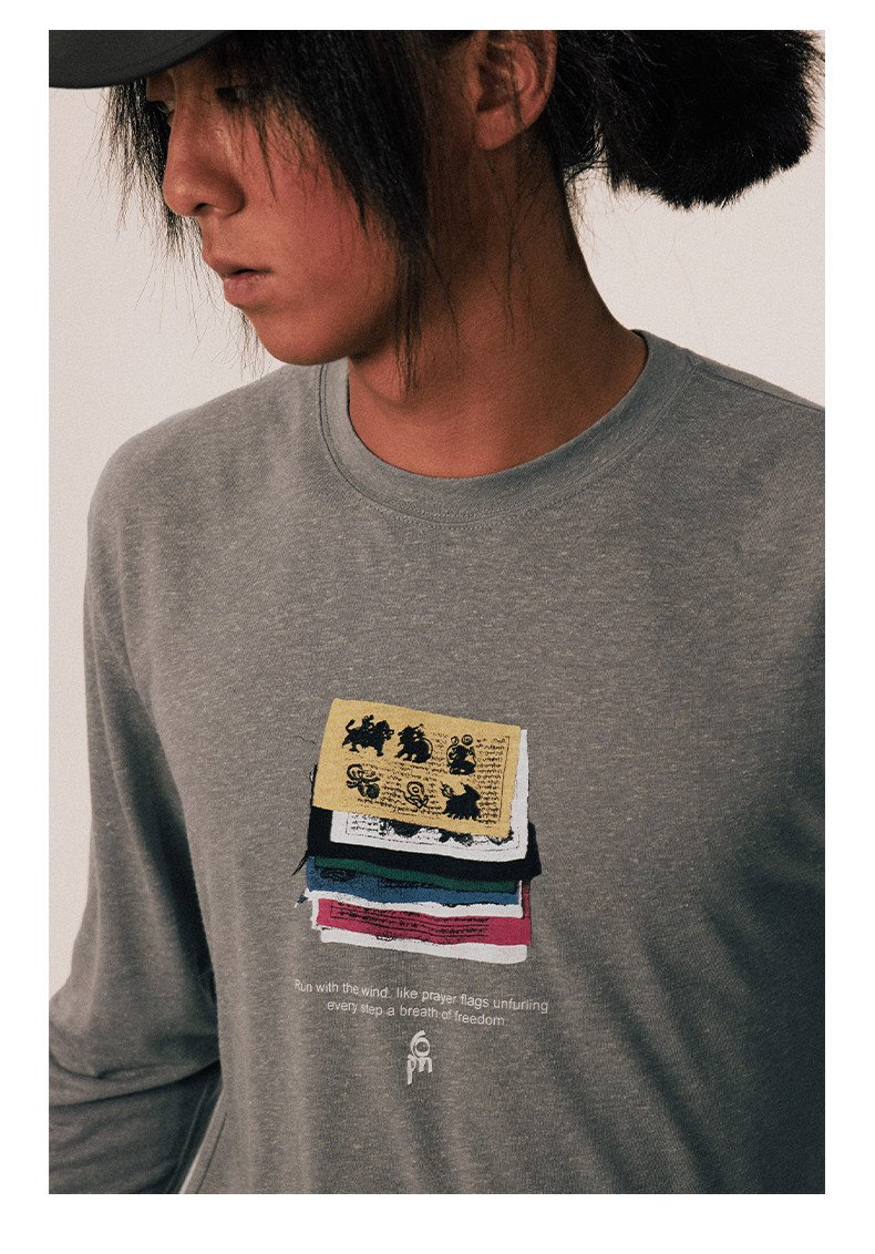 A person with long dark hair, partly covered by a hat, wears the EastLyst Vintage vintage T-shirt with stacked colorful animal patches and prayer flag-inspired text. The background is plain and light.