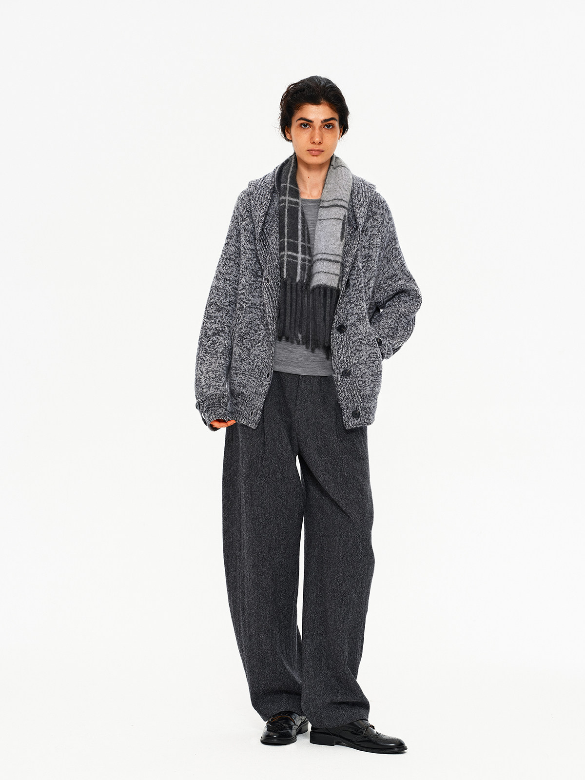 A person stands against a white background wearing a gray textured cardigan, gray shirt, wide dark gray trousers, and black shoes. They complete the minimalist look with EastLyst's Karl alpaca wool classic scarf.