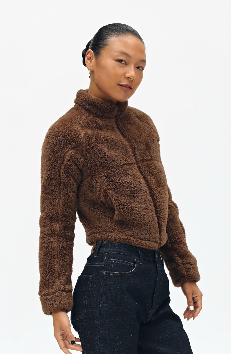 A person with slicked-back hair models the EastLyst Pink Short Faux Shearling Jacket and dark jeans, posing confidently against a plain white background.