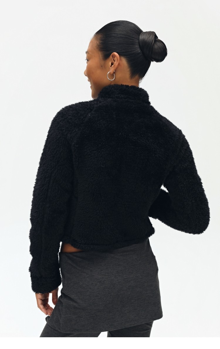 A person with dark hair in a bun is shown from the back against a plain, light background, wearing the EastLyst Pink Short Faux Shearling Jacket and dark pants.