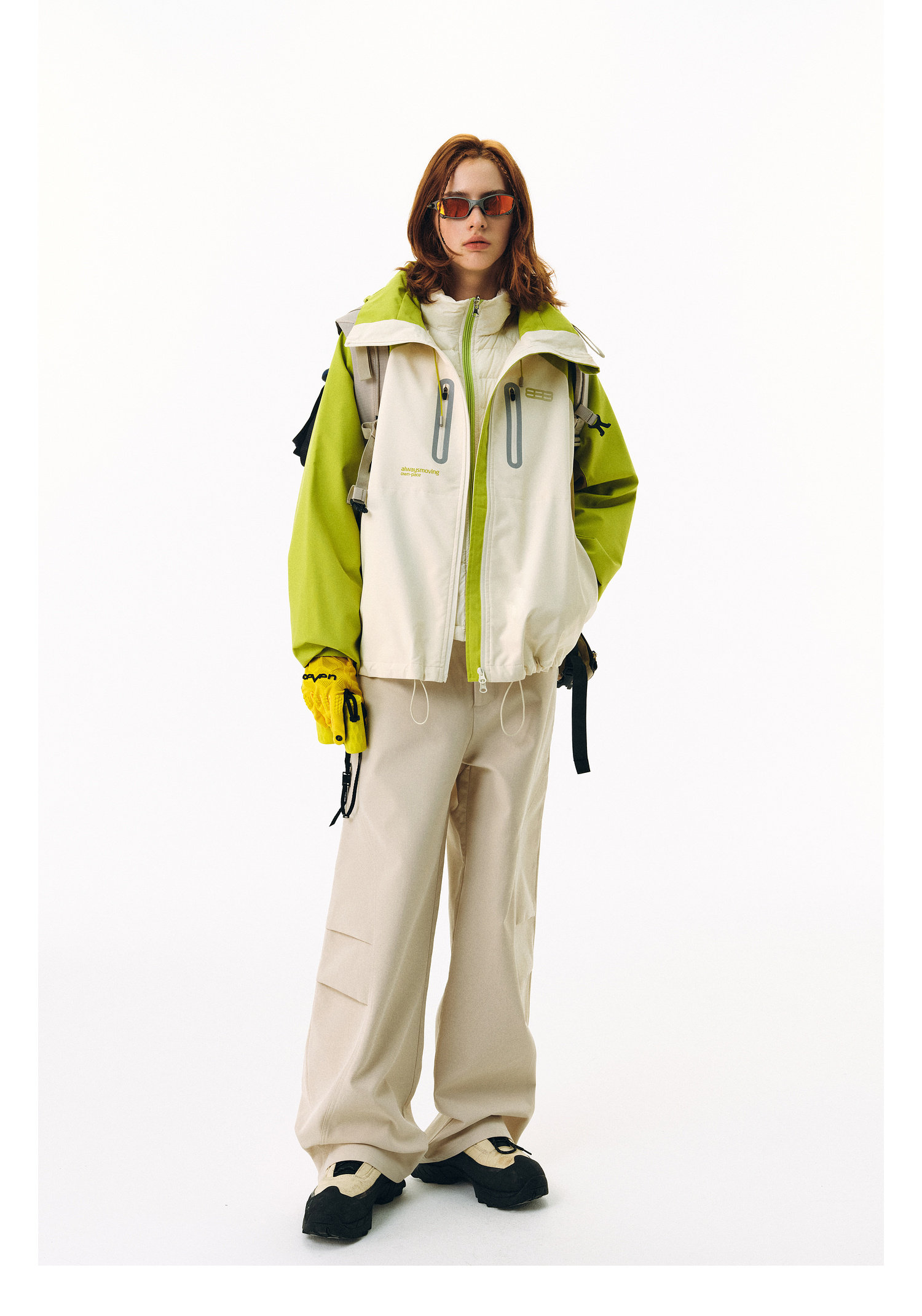 A person stands against a white background wearing the EastLyst Versatile Explorer 3-in-1 Jacket with green sleeves, matching wide-leg pants, yellow gloves, sunglasses, and black-and-white sneakers.