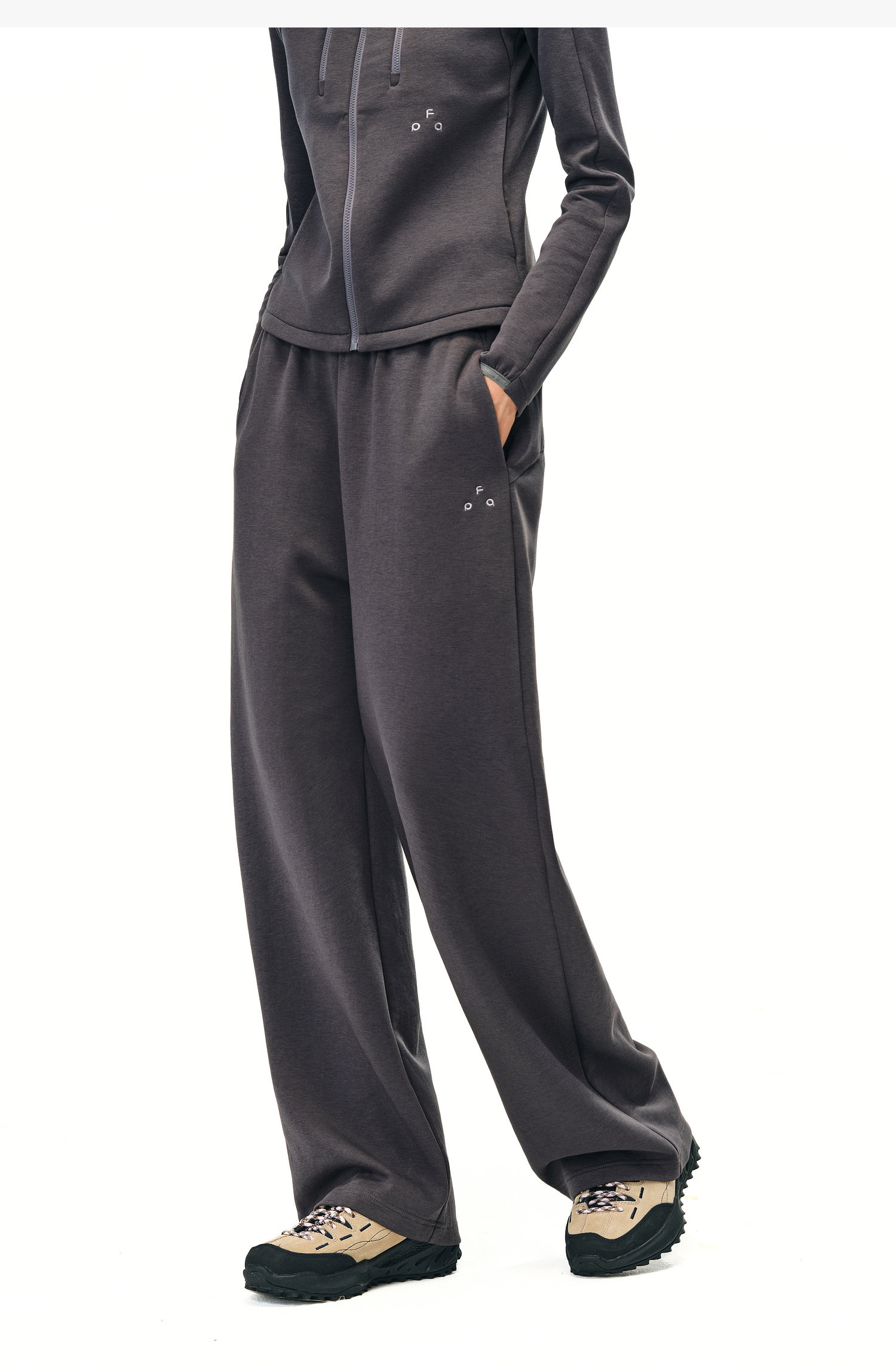 A person wears EastLyst Double-Layer Air-Knit Wide Leg Pants and a relaxed-fit dark gray zip-up hoodie, standing against a white background. The photo shows only their body from the shoulders down, paired with beige and black sneakers.