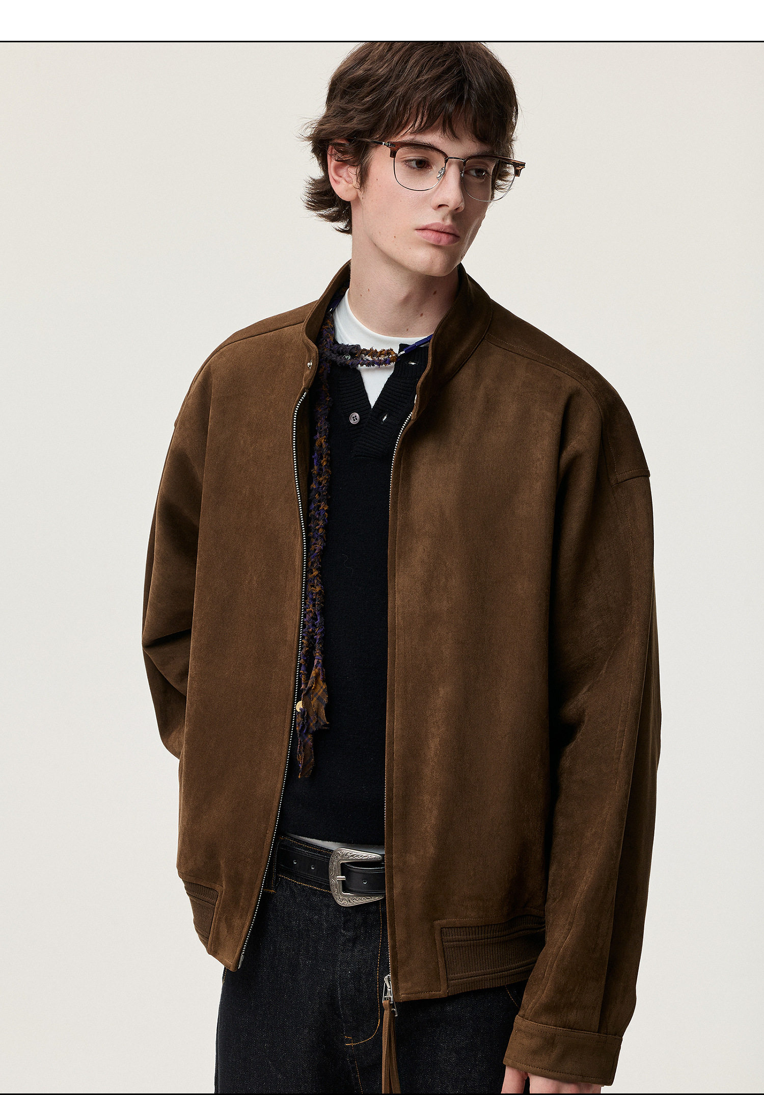 A young person with short brown hair and glasses wears the EastLyst Vintage Brown Harrington Jacket over a black shirt and dark jeans, standing against a plain light background, looking slightly to the side.