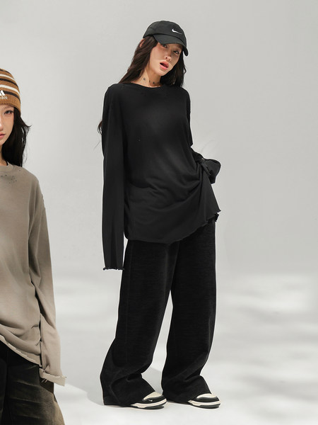 Woman modeling a loose black long-sleeve top, wide-leg pants, cap, and sneakers.