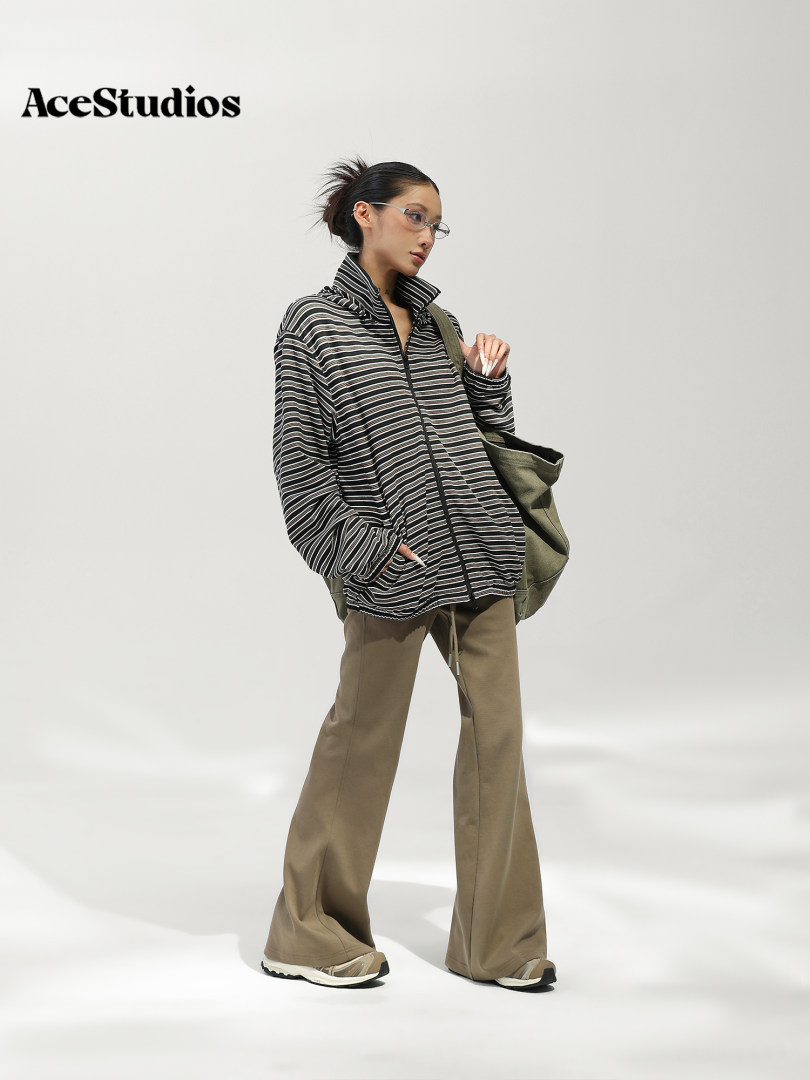 Model wearing a black-and-white patterned jacket with wide-leg trousers and carrying a large tote bag.