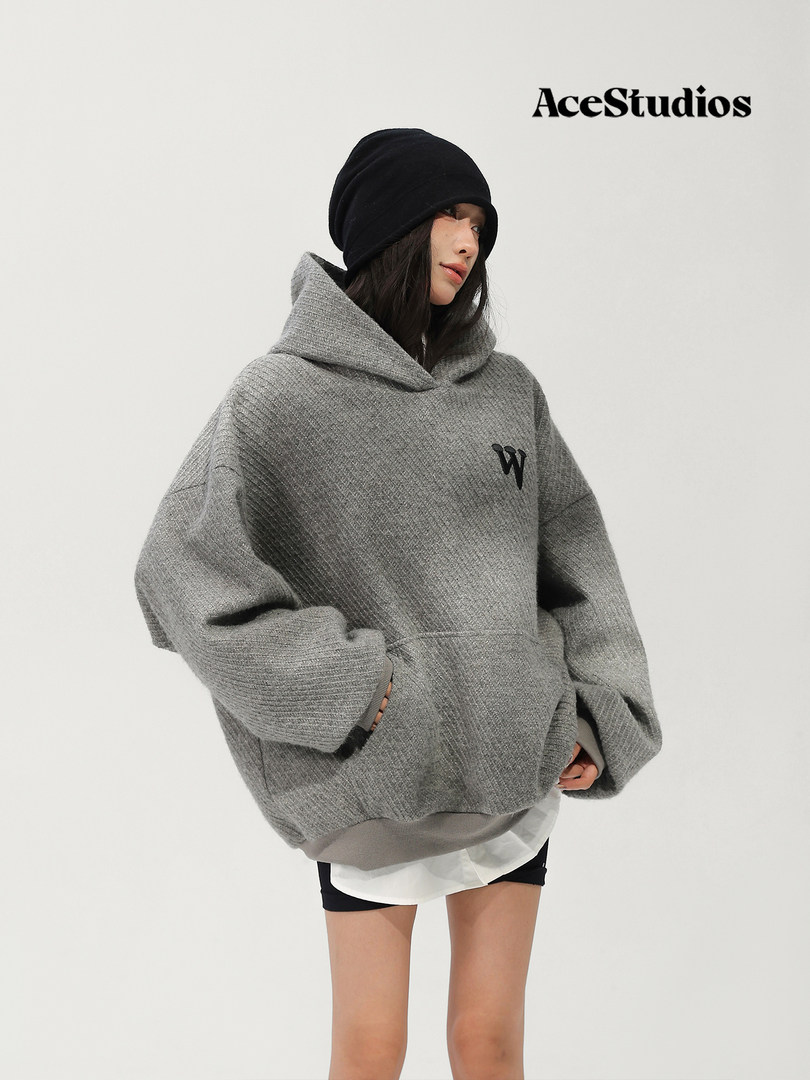 Model wearing an oversized gray hooded sweater with black beanie