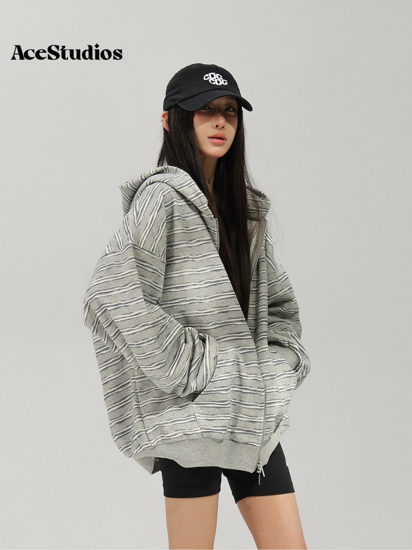 Model wearing a striped oversized hooded sweater with black shorts and a baseball cap.