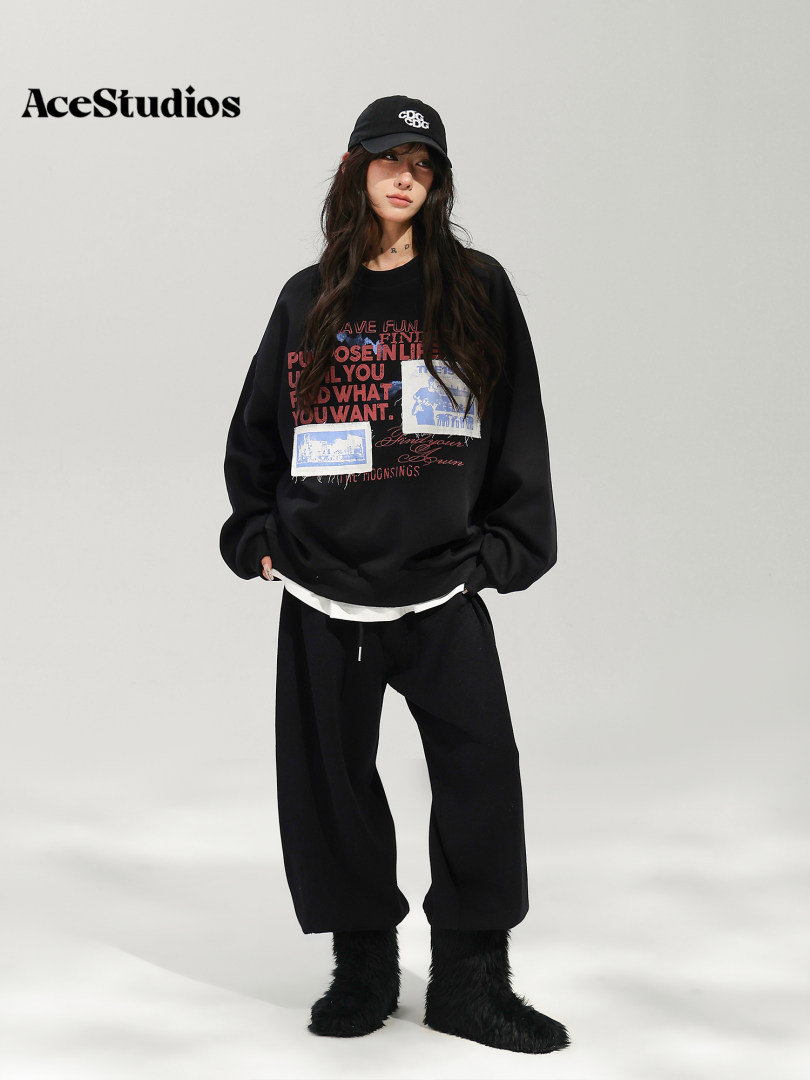Model wearing a black graphic sweatshirt, loose black pants, cap, and boots.
