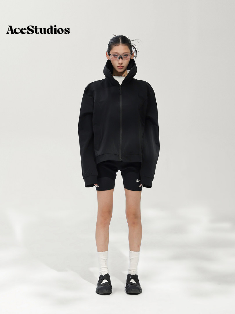 Model wearing a black zip-up hooded jacket with black shorts and sneakers.