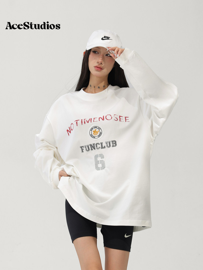 Model wearing an oversized white graphic sweatshirt with black athletic shorts and a white cap.