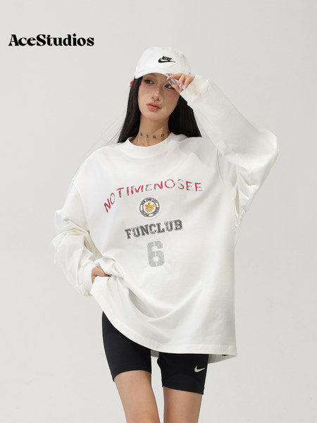 Model wearing an oversized white graphic sweatshirt with black athletic shorts and a white cap.
