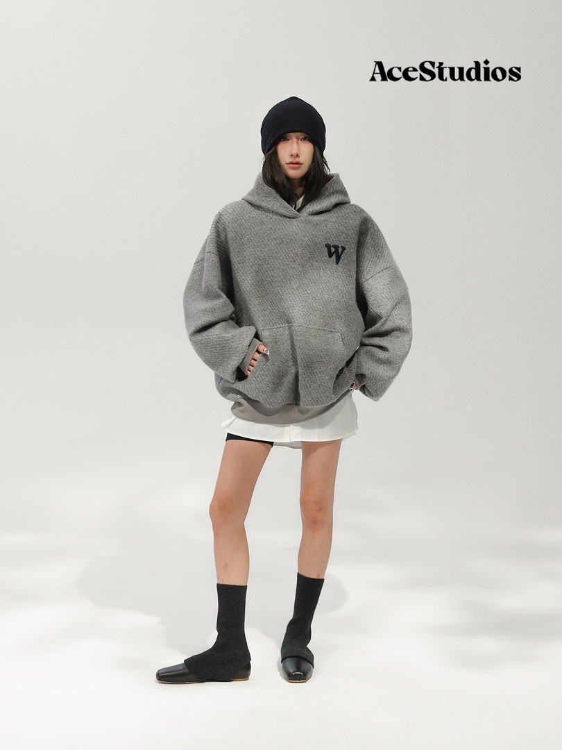 Model wearing an oversized gray knitted hooded sweater with a black beanie and socks.