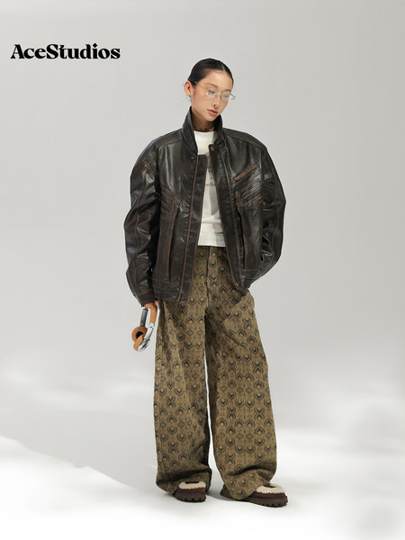 Model wearing a black leather jacket, white top, patterned wide-leg trousers, and sandals.